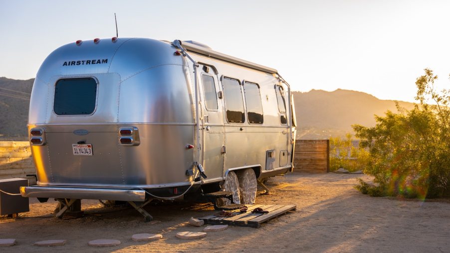 Silver Airstream camper trailer, with the sun setting over mountains in the background.