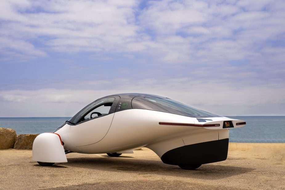 A white Aptera parked in front of an ocean.