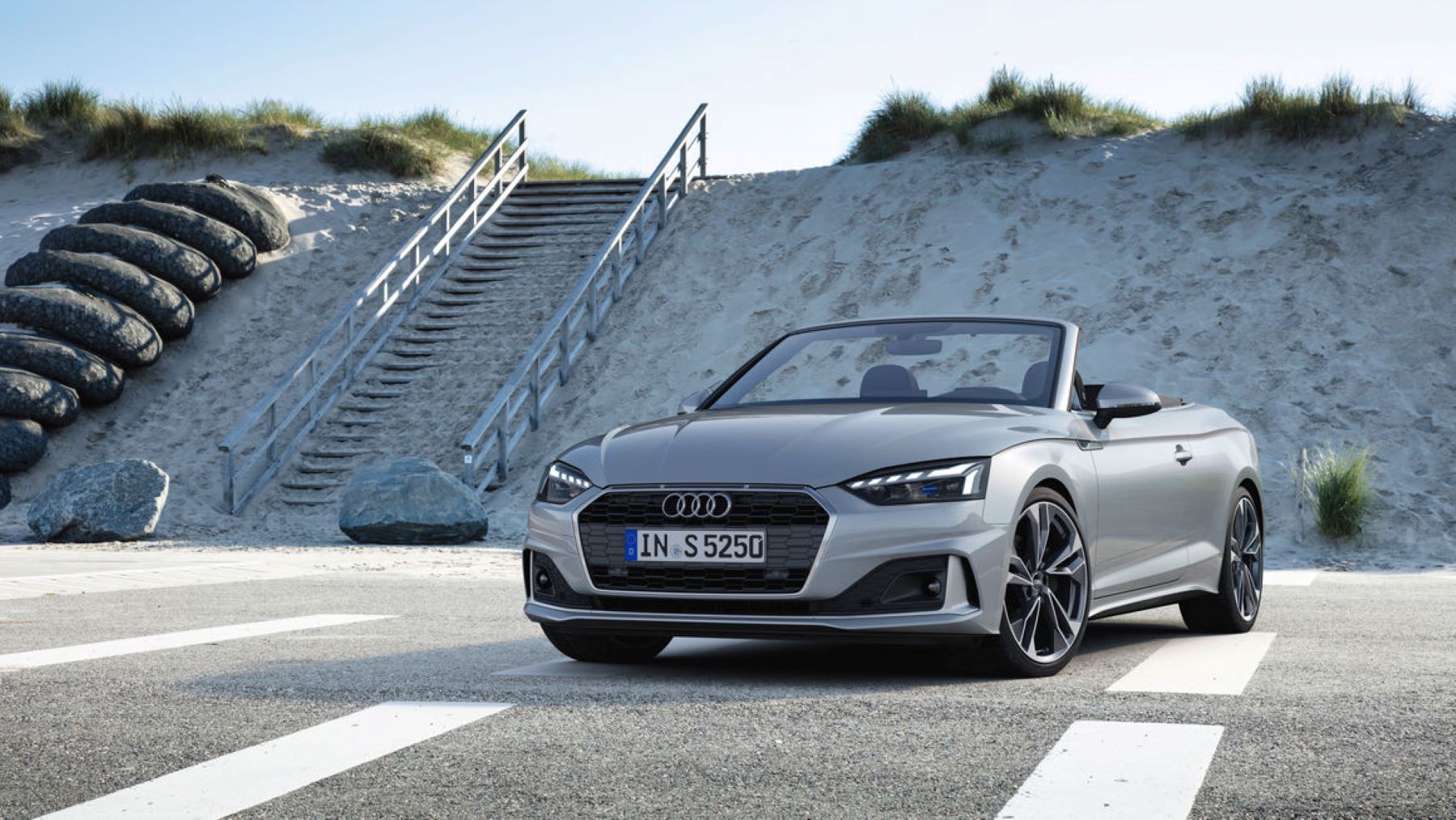 A silver gray Audi A5 convertible convertible in a parking lot next to a beach with stairs