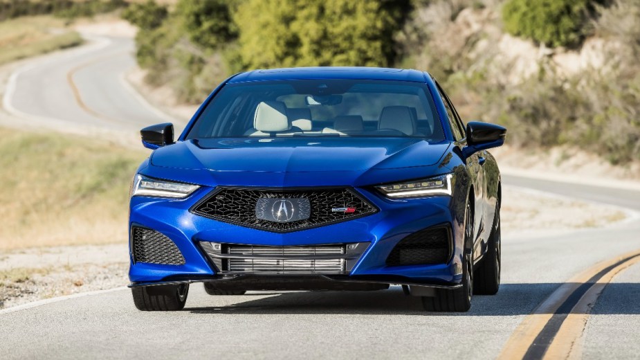 The front grille view of a blue Acura TLX Type S driving on a scenic road. 