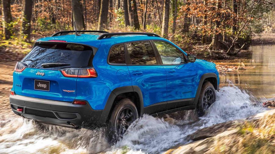 A blue 2022 Jeep Cherokee splashing through a puddle.