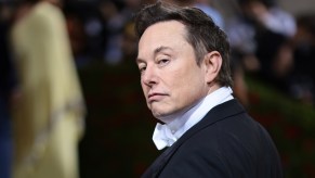 Elon Musk dressed in a black suite and white collar.
