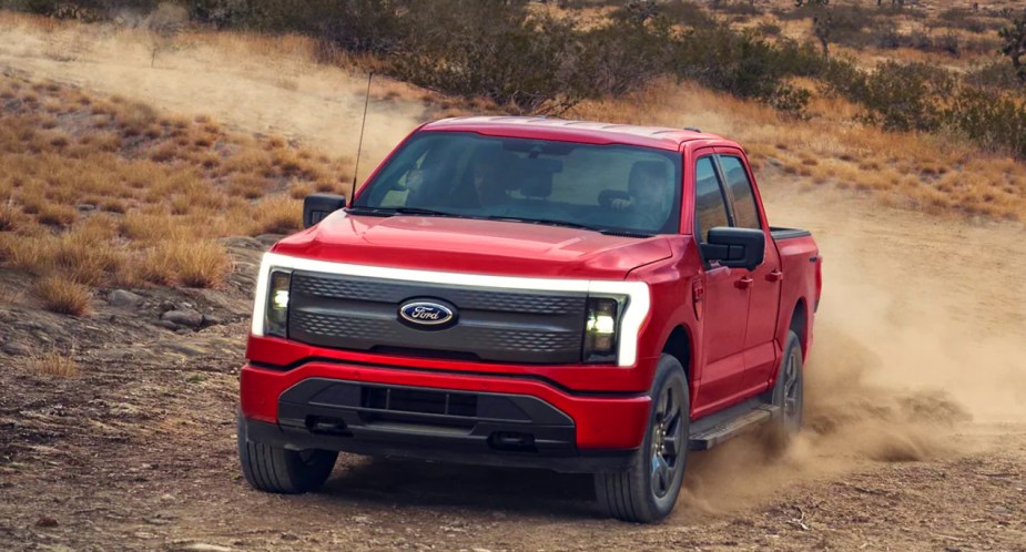 A red 2022 Ford F-150 Lightning electric pickup truck is driving off-road. 