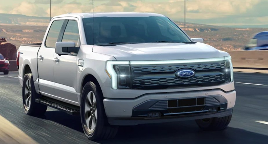 A gray 2022 Ford F-150 Lightning electric pickup truck is driving on the road.