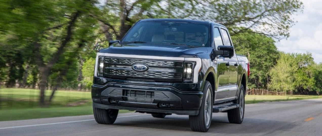 A black 2022 Ford F-150 Lightning Platinum is driving on the road.