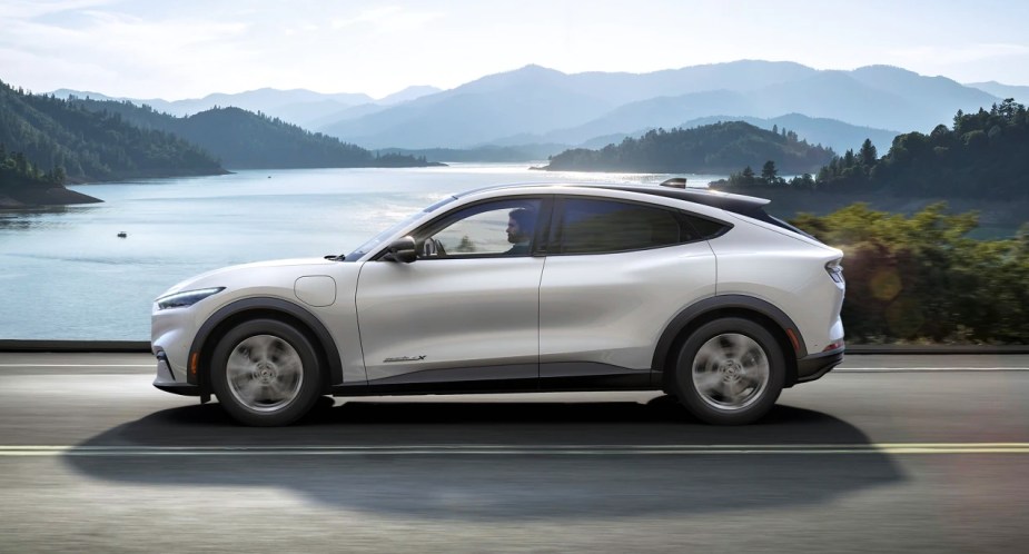 A white 2022 Ford Mustang Mach-E electric SUV is driving on the road. 
