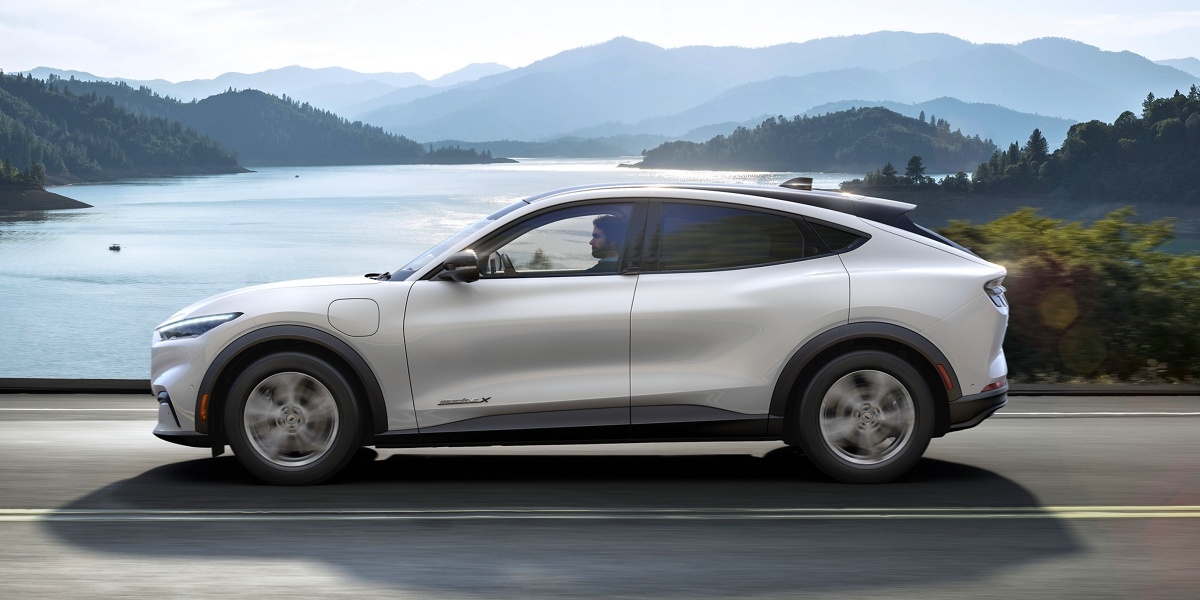 A white 2022 Ford Mustang Mach-E small electric SUV is driving on the road.