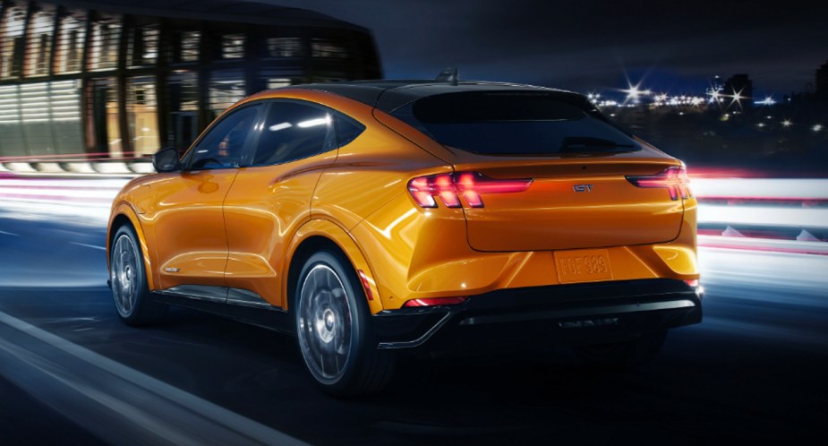 An orange 2022 Ford Mustang Mach-E electric SUV is driving down the road.
