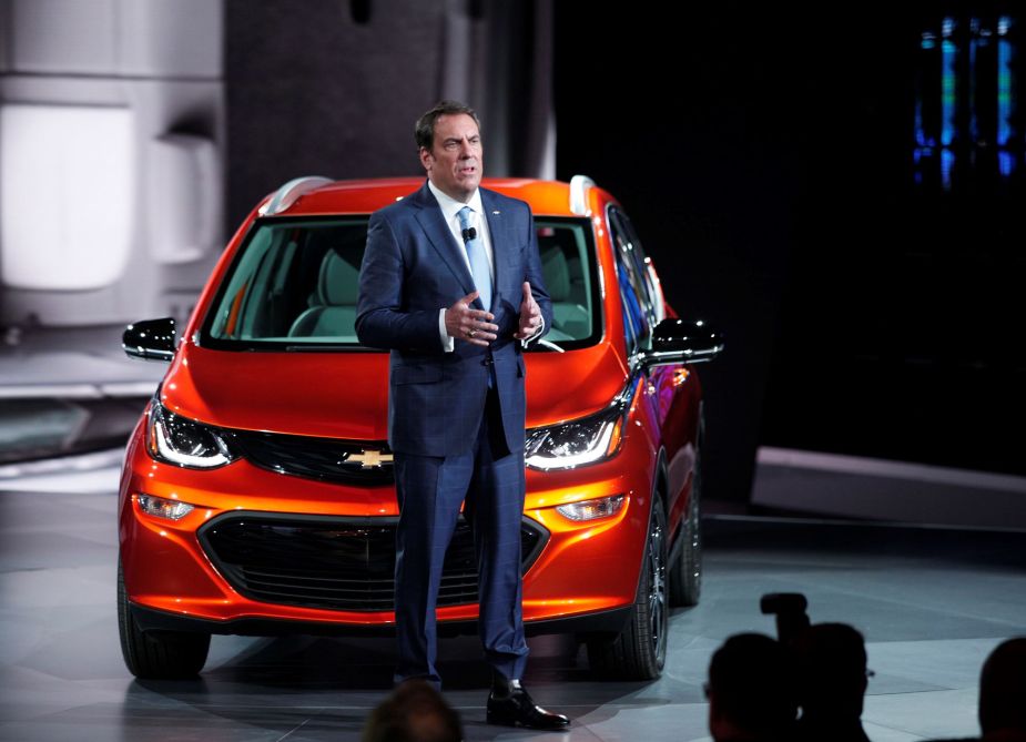 GM president Mark Reus standing in front of an orange Chevy Bolt. 