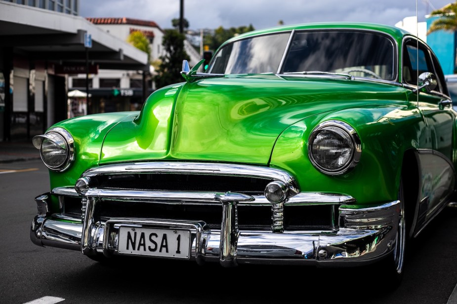 The chrome bumper of a restored classic car painted a custom green color.