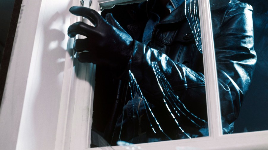 A burglar reaching through a smashed window pane to open a latch.