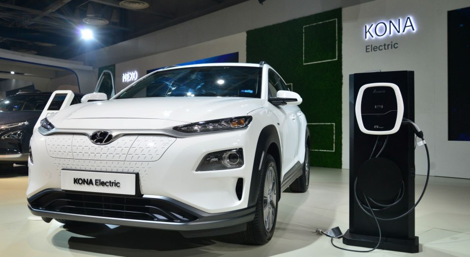 `A white Hyundai Kona indoors next to a charger. 