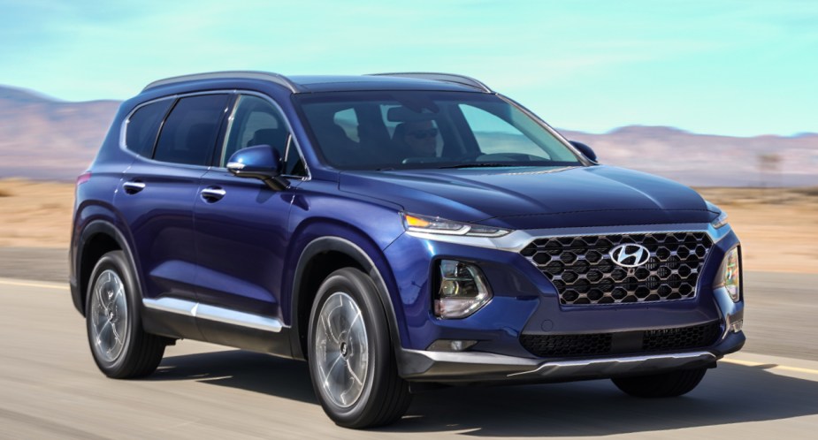 A blue 2019 Hyundai Santa Fe midsize SUV is driving on the road. 