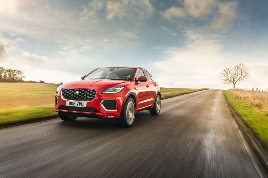 A red 2022 Jaguar E-Pace P300E PHEV luxury SUV model driving through the country under a cloudy sky