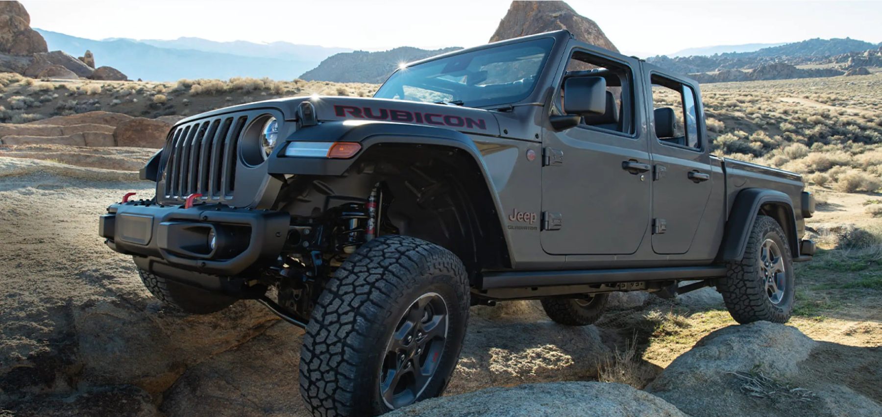 A 2022 Jeep Gladiator Rubicon midsize pickup truck climbing over rocks and boulders off-road