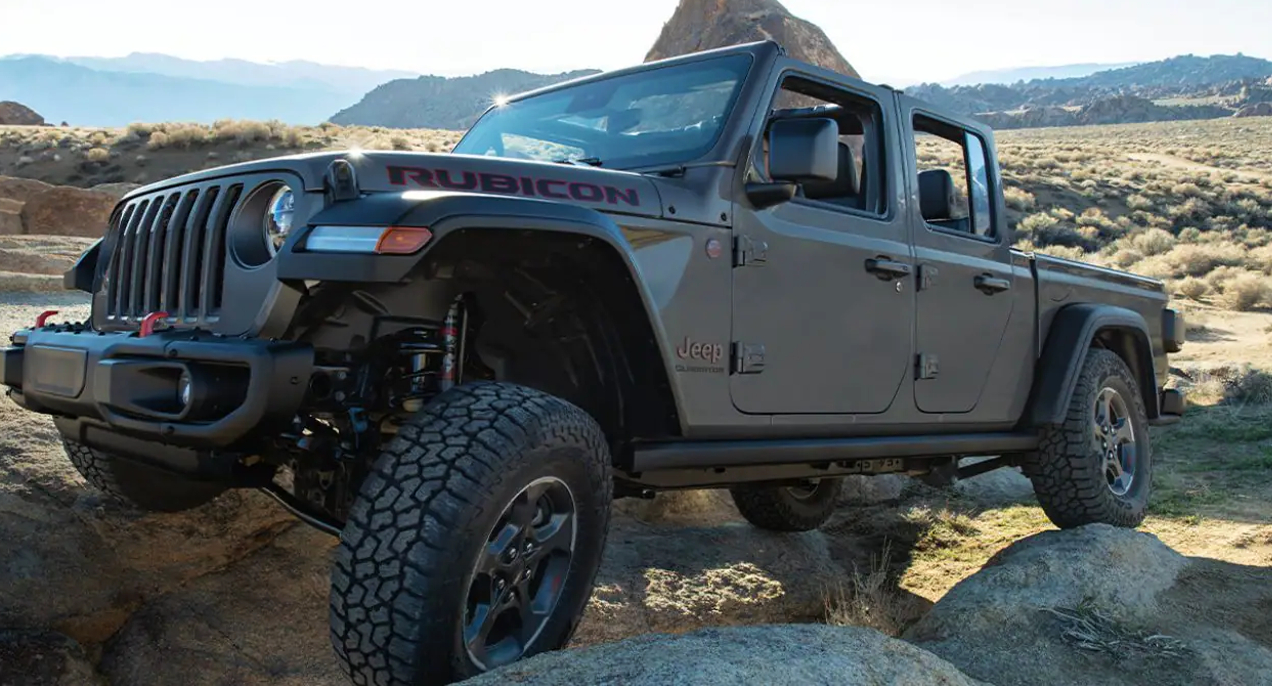 A gray 2022 Jeep Gladiator off-road pickup truck is driving on rocks.
