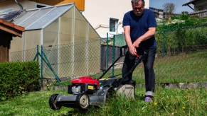 A person pushing a lawn mower, that could be across uneven ground.