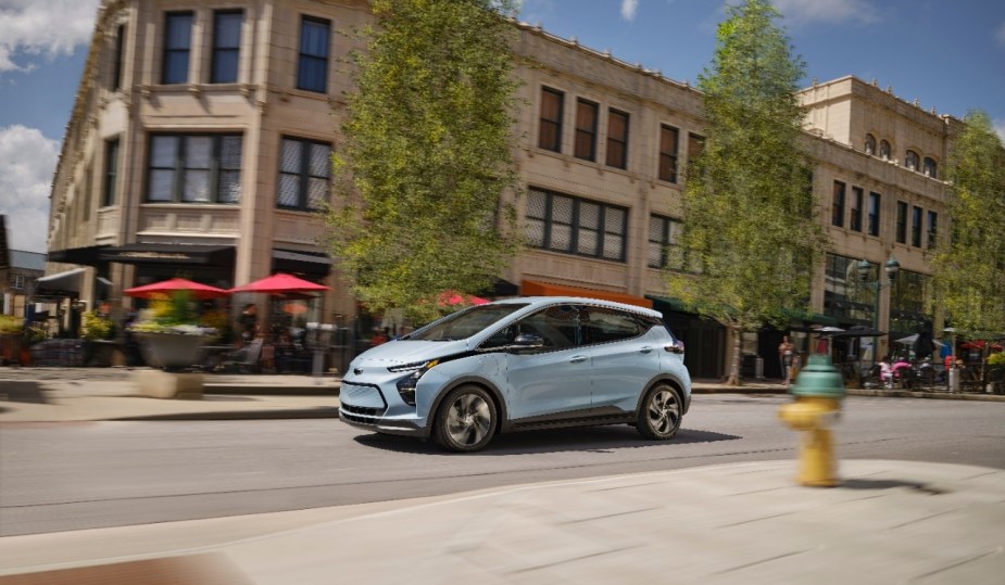Light blue 2023 Chevy Bolt EV driving on a city street, highlighting its release date and price
