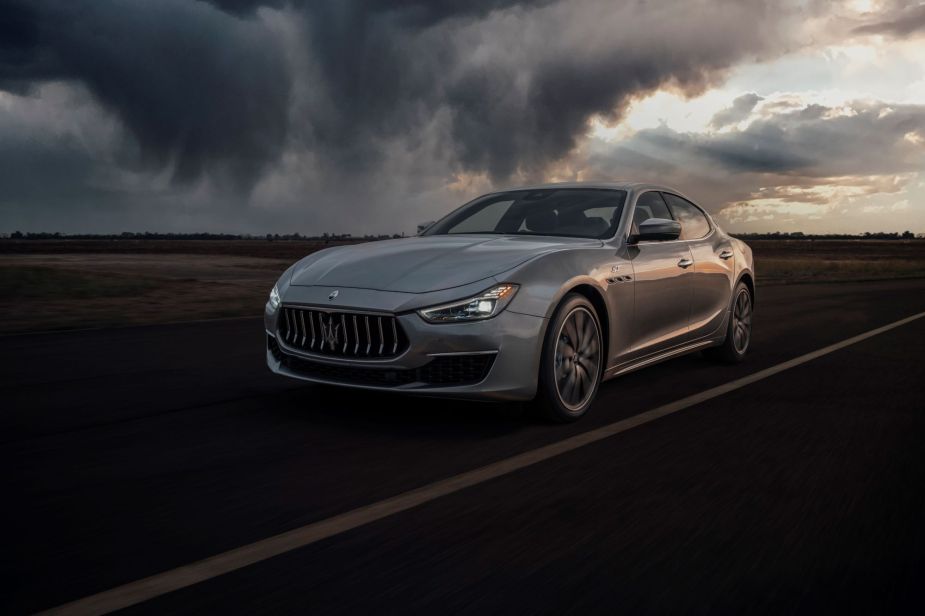 A grey Maserati Ghibli, the worst midsize luxury car, driven down the road. 