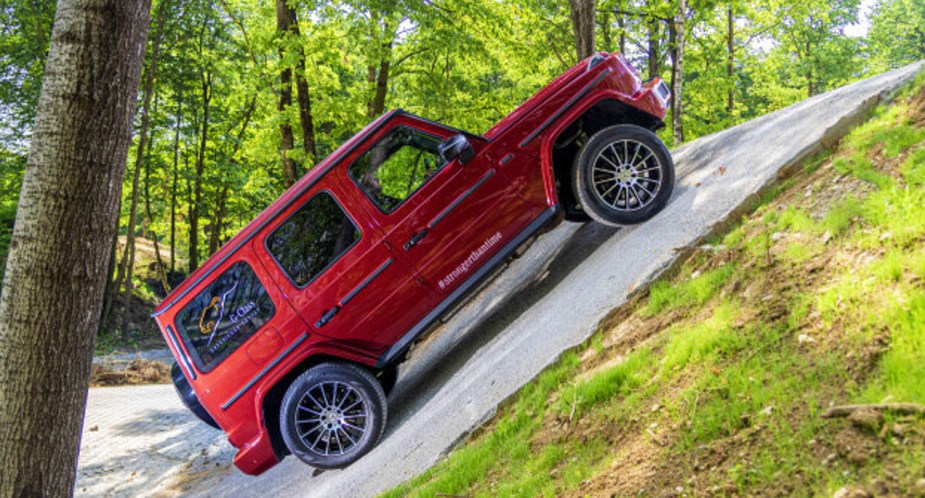 A red 2022 Mercedes-Benz G-Class luxury midsize SUV is driving up a steep hill. 