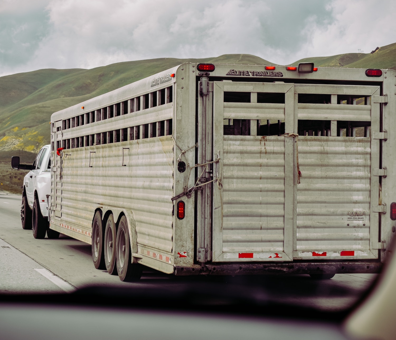 Heavy-duty Ram pickup truck twoing a heavy livestock trailer down the interstate, rolling hills visible in the background.