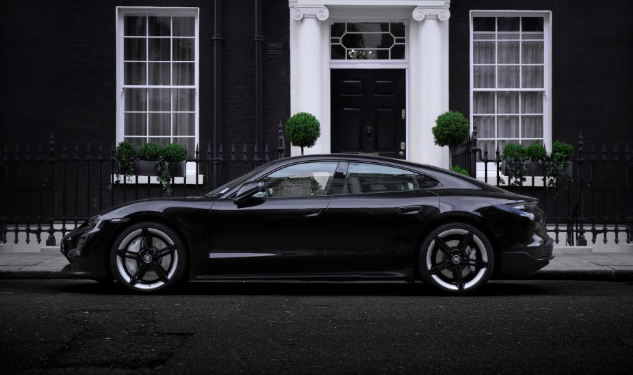 A black Porsche Taycan parked in front of a black building. 