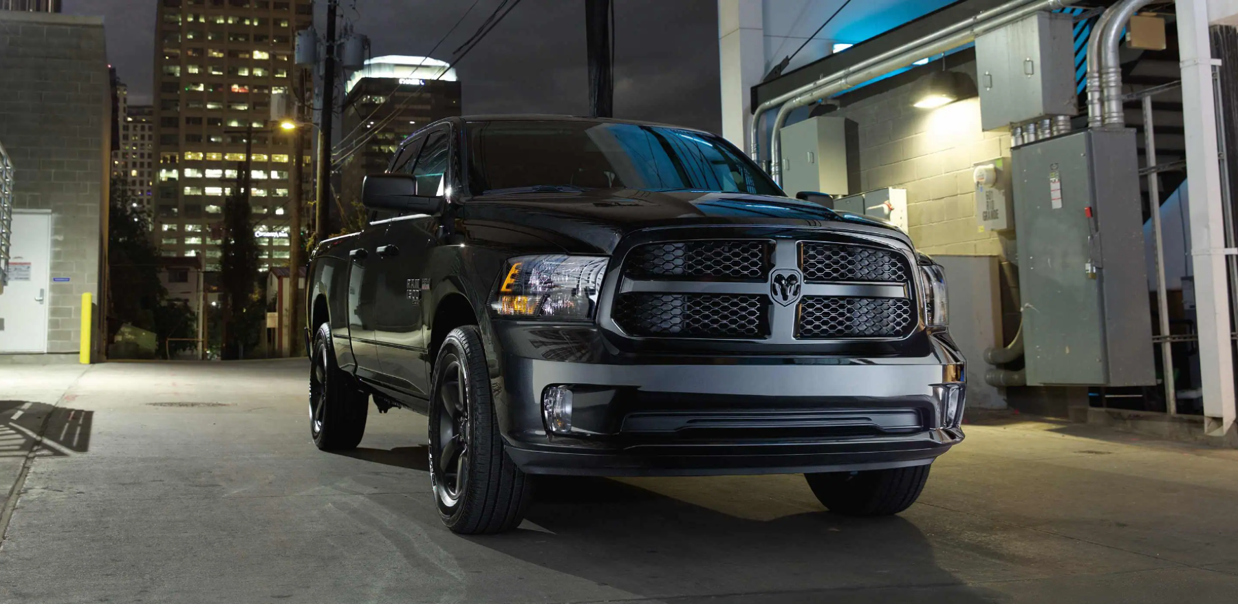 A black and gray Ram 1500 Classic full-size pickup truck parked near electrical maintenance equipment in a city at night