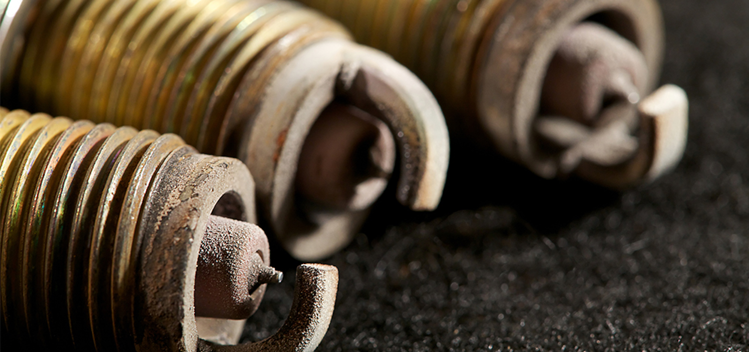 Closeup of sooty, sandy deposits on the electrodes of three spark plugs.
