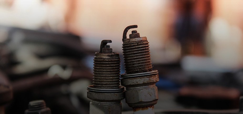 Closeup of used spark plug electrodes covered in soot and other deposits, in front of a blurry background.