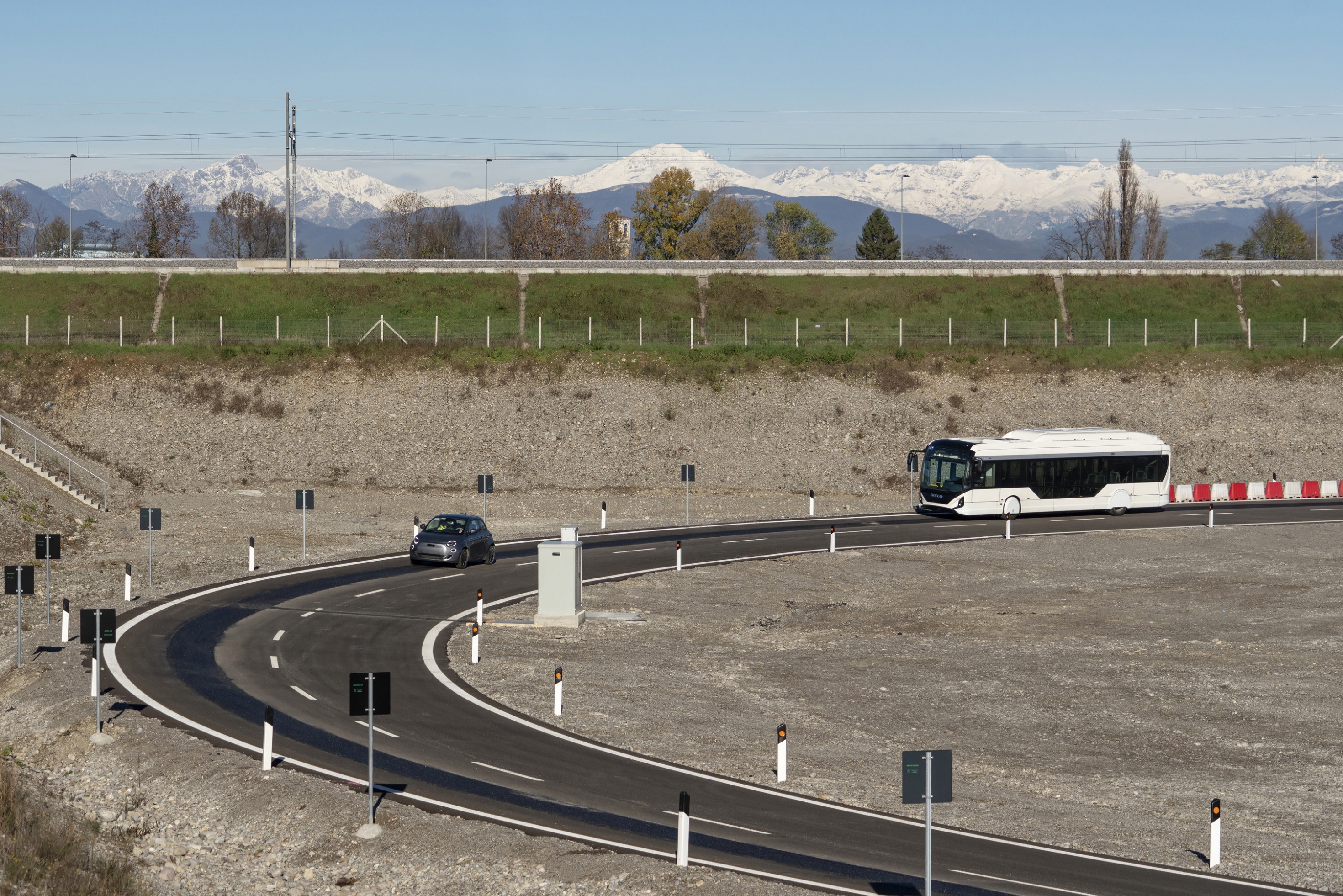 A gray Fiat 500 EV and white bus running on Stellantis' Italian test track testing a new wireless charging system