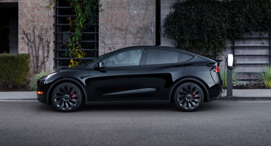 A black 2022 Tesla Model Y electric SUV is parked and charging. 