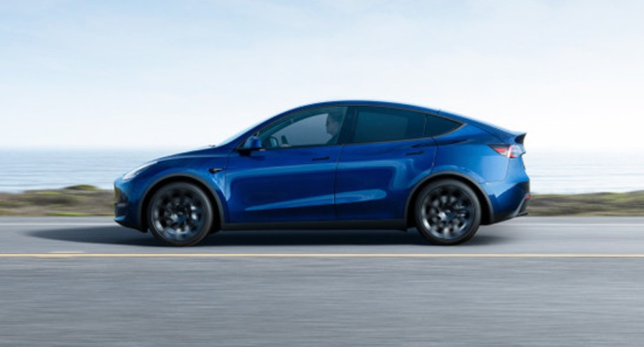 A blue 2022 Tesla Model Y electric SUV is driving on the road. 