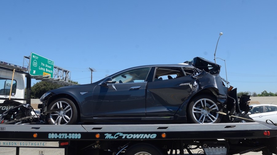 A gray colored Tesla SUV on a flatbed trailer after being rear-ended.