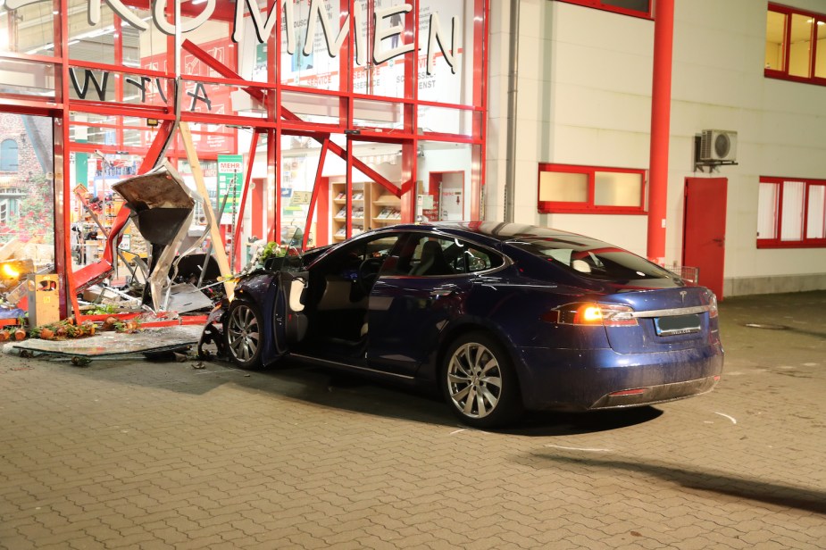 A blue Tesla sedan smashed into a store front in an night time parking lot.