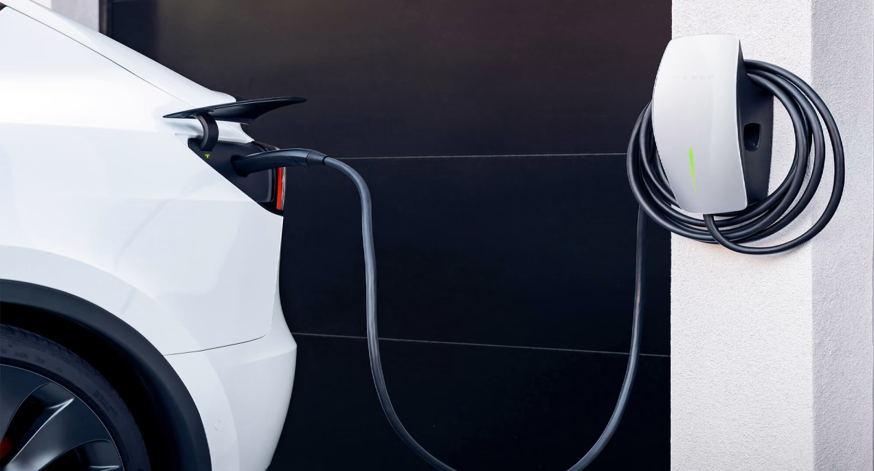 A white Tesla is plugged into a Tesla Wall Connector home charger.