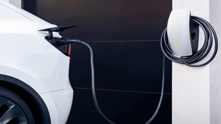 A white Tesla is plugged into a Tesla Wall Connector home charger.