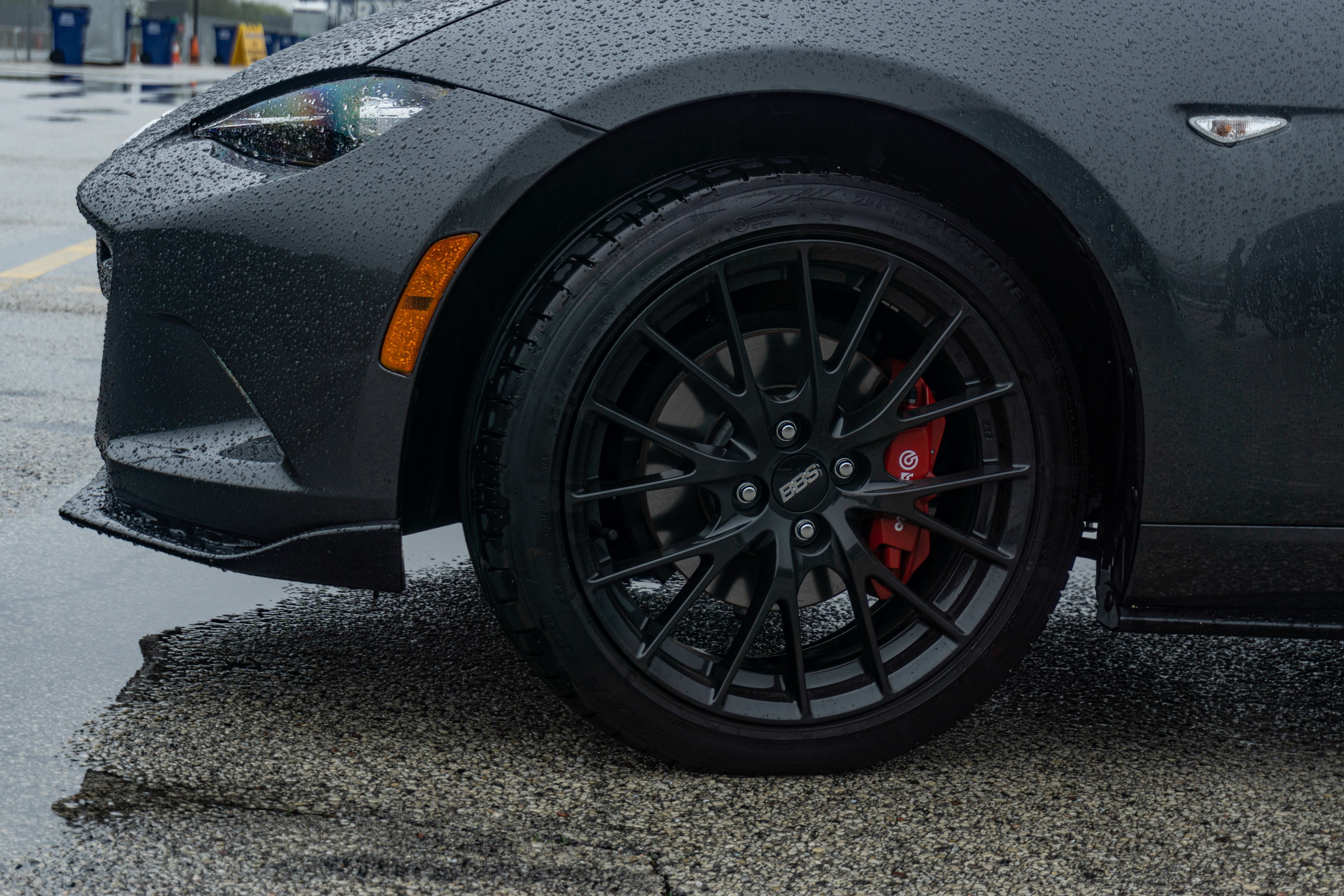 The front black BBS wheel and red Brembo brake caliper of a gray 2022 Mazda MX-5 Miata RF Club in a racetrack parking lot