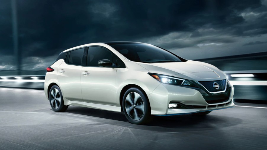 A white 2022 Nissan Leaf electric car is driving on the road.