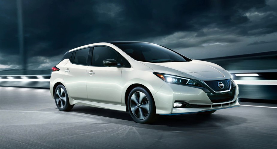 A white 2022 Nissan Leaf electric car is driving . 