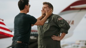 Tom Cruise and James Corden standing out side with Cruise's hands on Corden's face in front of a jet.