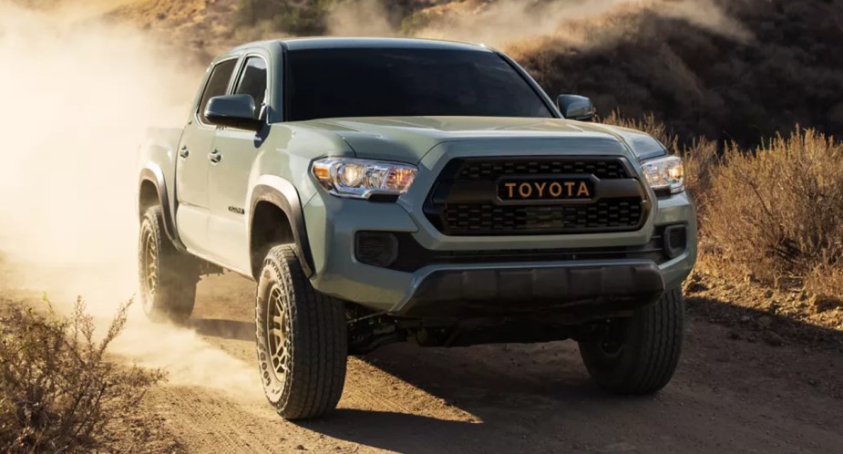 A green Toyota Tacoma midsize pickup truck is driving off-road. 