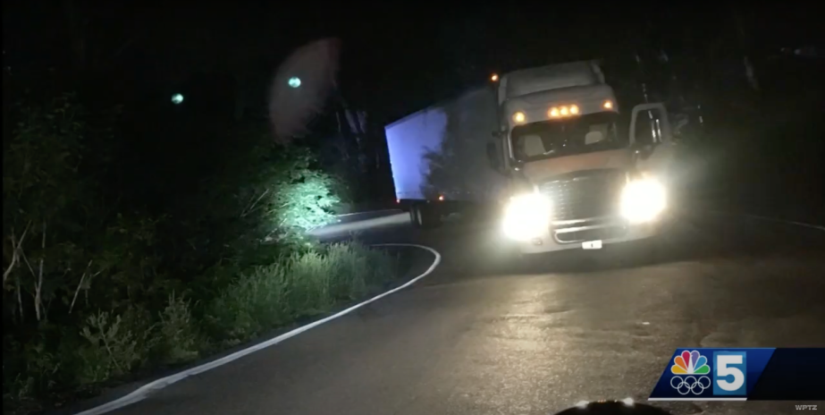 Truck abandoned in a mountain pass at night with its door open and headlights left on.
