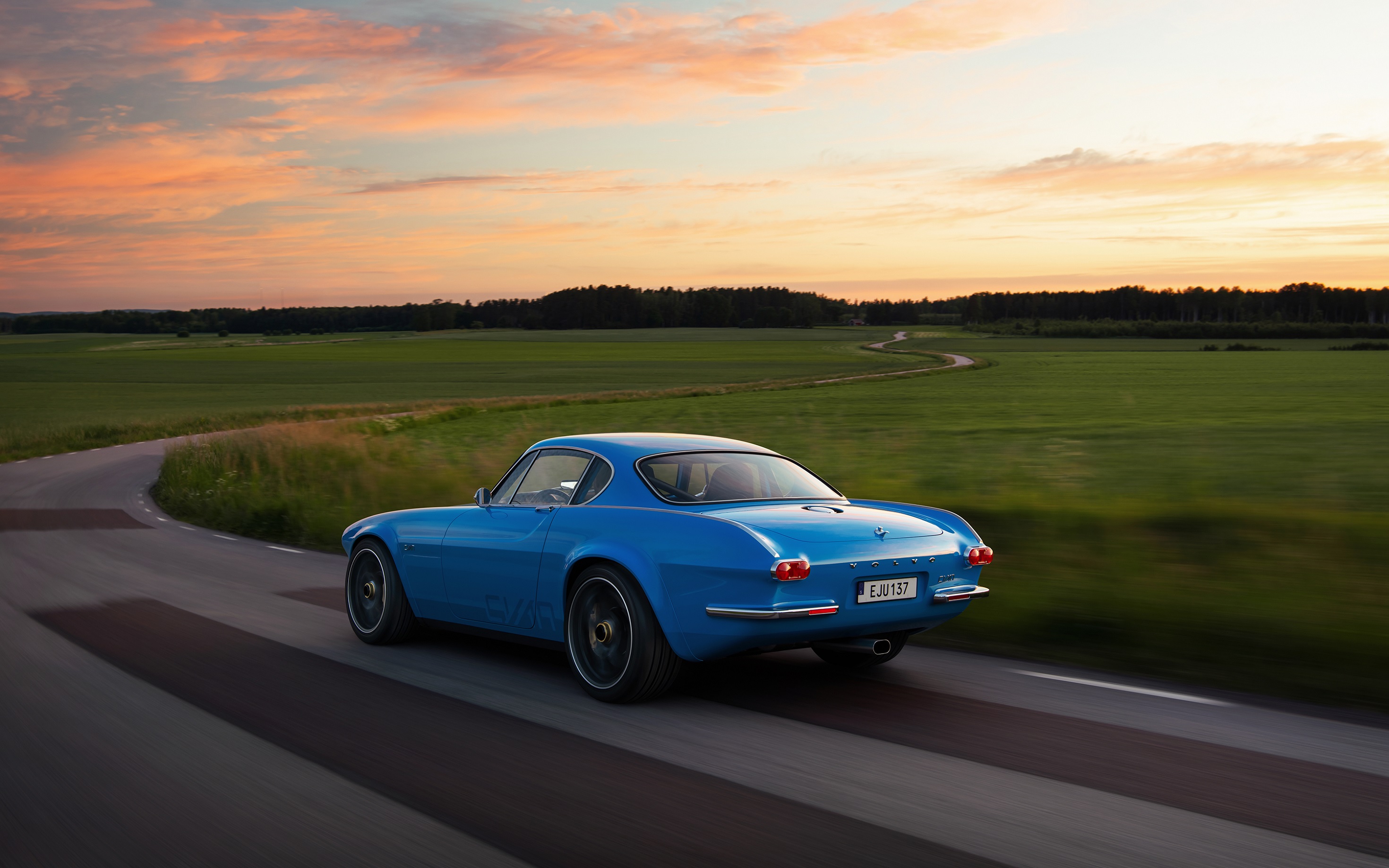 The rear 3/4 view of a blue Volvo P1800 Cyan driving on a country road