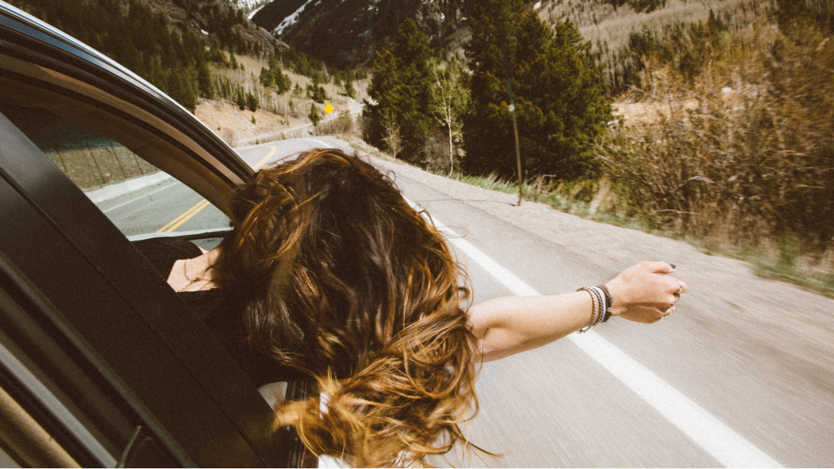 a woman leans out a window enjoying the open road and the road trip