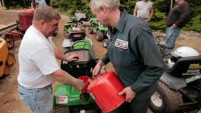 Mike Ramsey holding a funnel as Dan Bowley pours gasoline into a lawn mower at the Saco Pathfinder Snowmobile Club