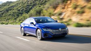 A blue 2022 Volkswagen Arteon executive car model driving on a highway near a cliffside of trees