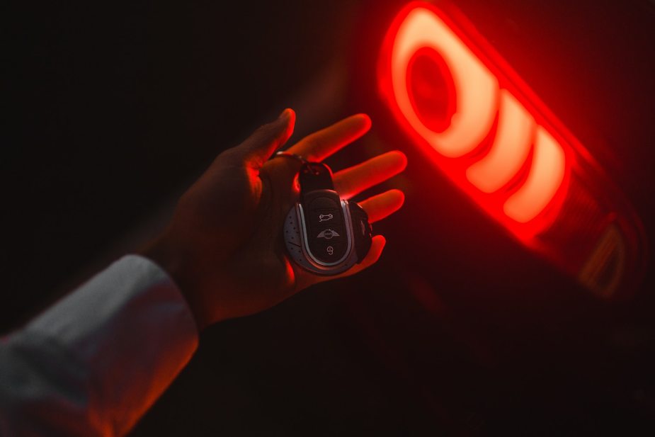 A hand holding a key fob near a car's lit brake lights.