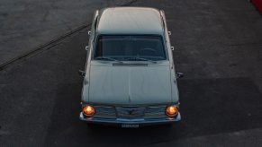 Plymouth valiant classic car parked on the pavement at twilight with its headlights on.