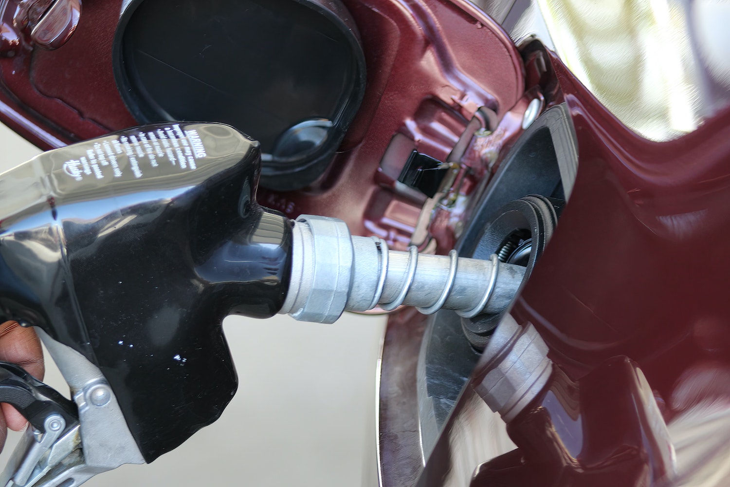 Closeup of a driver's hand pumping gas into the half full tank of their car.