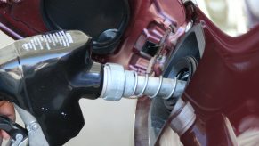 Closeup of a driver's hand pumping gas into the half full tank of their car.